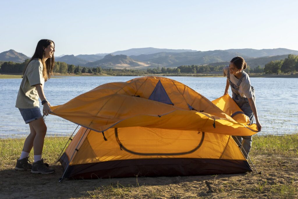 two girls setting up pop up tent near lake